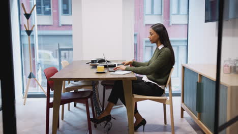 Businesswoman-Working-On-Laptop-And-Using-Mobile-Phone-At-Desk-In-Meeting-Room