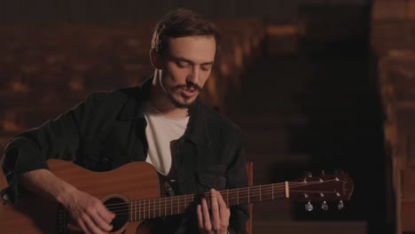 un chico guapo toca una guitarra acústica en un cine abandonado. el músico canta una canción y acompaña en la guitarra
