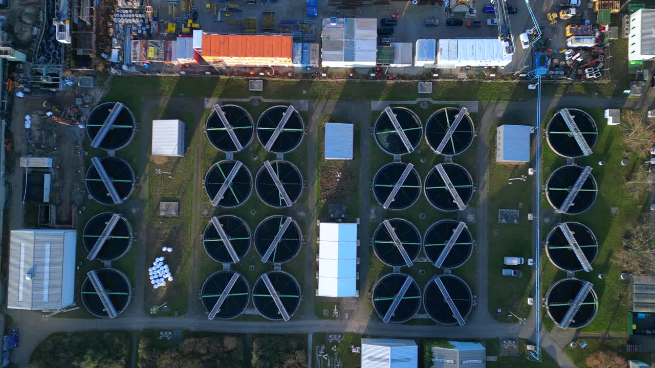 Industrial complex with a chimney emitting smoke into the sky, next to a sewage treatment facility and urban infrastructure. Amazing aerial view vertical bird's eye view drone top down Above view