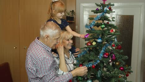 Children-girl-with-grandparents-couple-decorating-artificial-Christmas-pine-tree-at-old-fashion-home