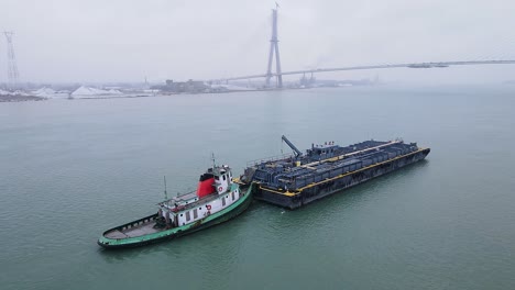 tugboat pushes industrial barge near gordie howe bridge on cloudy river morning