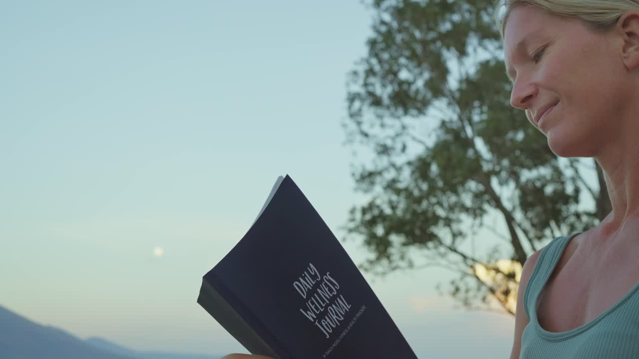 여성은 보름달이 있는 해가 뜨는 동안 야외에서 생각을 일기적으로 기록합니다.