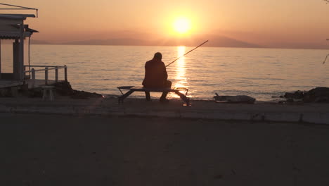 Alter-Fischer-Sitzt-An-Der-Promenade-In-Der-Zeitlupe-Des-Sonnenuntergangs