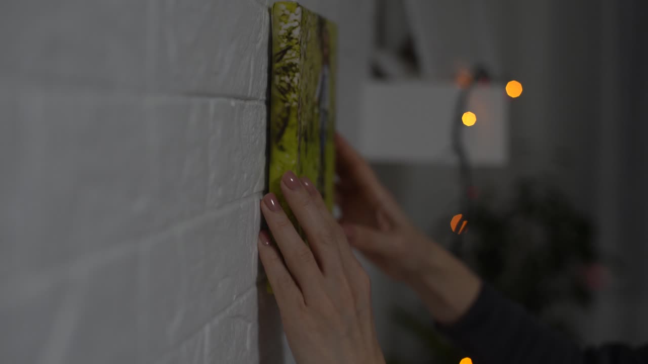 한 여성이 벽에 사진 캔버스를 매달고 있다.