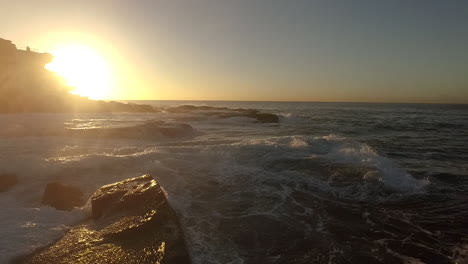 a dramatic drone shot in slow motion flying through the spray of waves crashing on the rocks at bondi shortly after sunrise