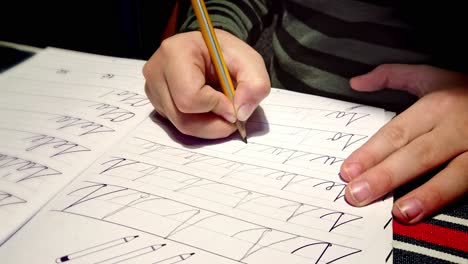 Child-sitting-at-table-practicing-joined-up-writing-homework-repetition-in-lined-notebook-close-up