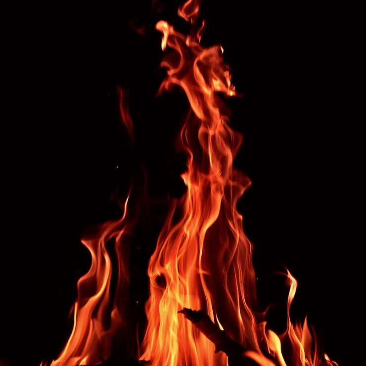 Bastoncini di legno che bruciano in un grande falò. Lunghe lingue di fuoco che si estendono alte nell'aria. Sfondo nero