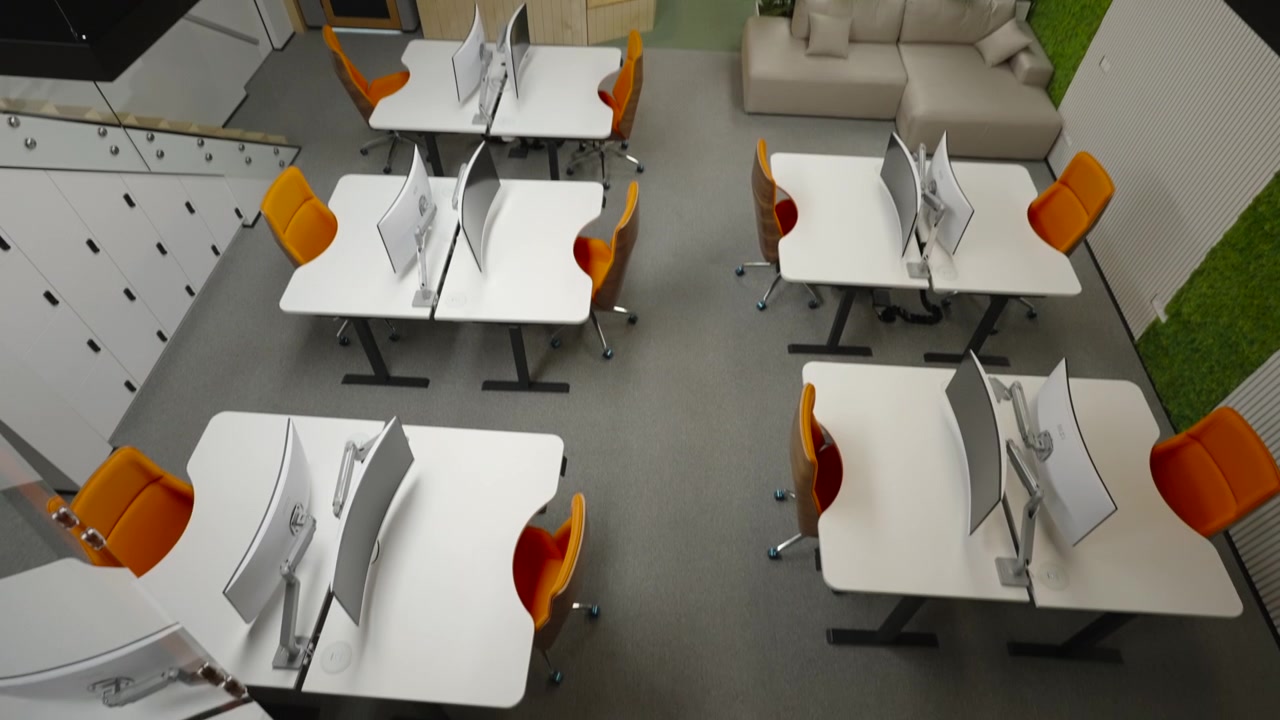 Bright contemporary office space with white desks, computer monitors, orange chairs, indoor plants, a comfortable sofa, and a mezzanine seating area under