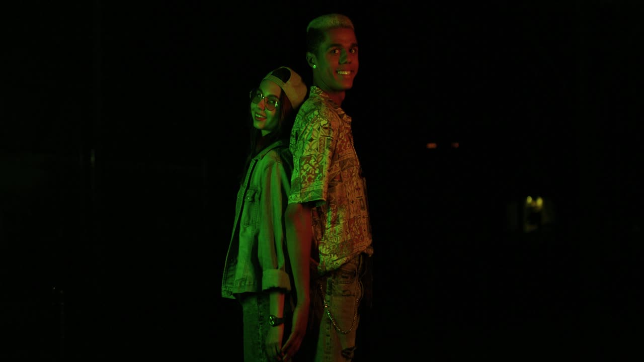 adolescente afroamericano y caucásica con gafas y gorra tocándose la espalda y mirando la cámara