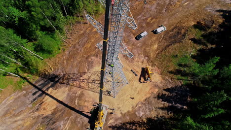 aerial top down shot of workers installing new transmission tower with crane in forest