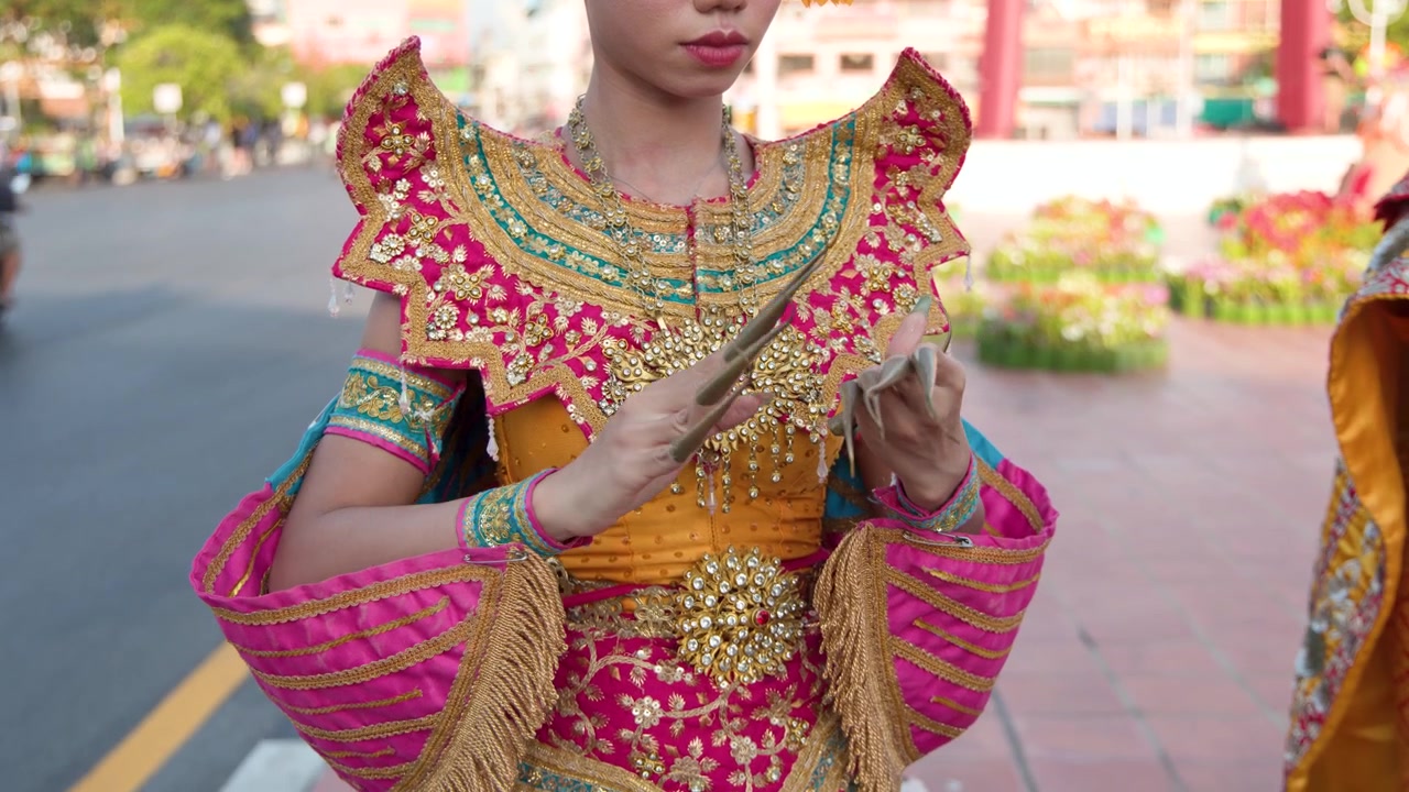 Una bailarina tailandesa con un elaborado traje dorado se ajusta las largas uñas metálicas durante el día en Bangkok.
