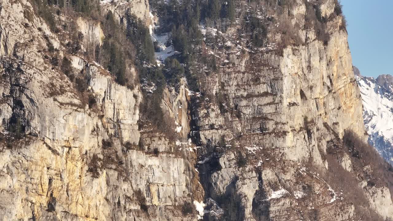 Aerial view of rocky cliffs towering over the landscape of Amden, Switzerland, with traces of snow clinging to the steep rock faces. The rugged beauty of the cliffs.