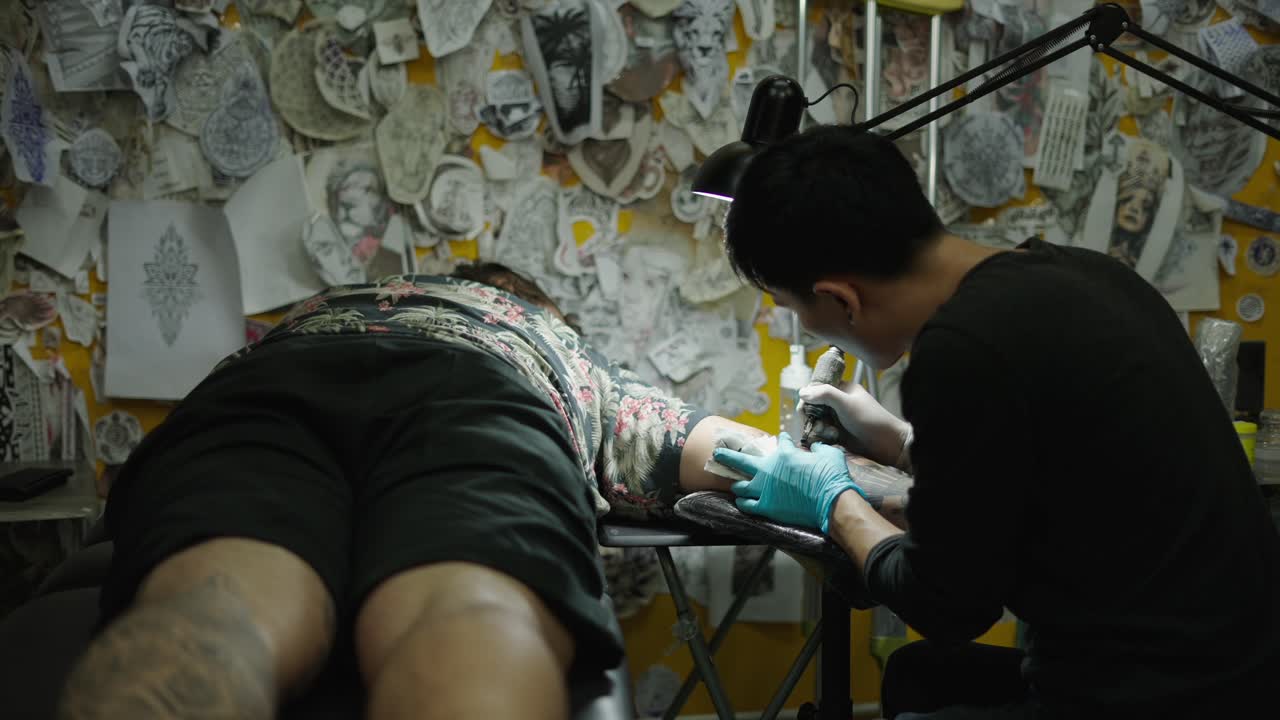 Tattoo artist working on a client's arm in a studio
