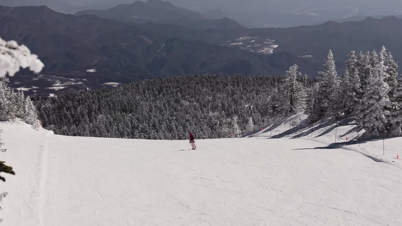 Skiers riding down wide snowy slope overlooking distant mountain range