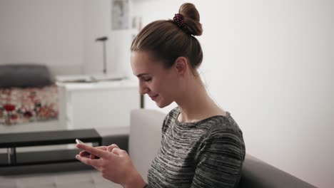 portrait of a happy young woman sitting on the couch at home looking at phone and typing a message