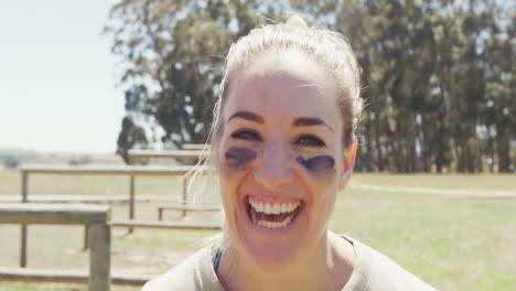 Portrait-of-smiling-female-soldier-wearing-eye-black-standing-in-field-on-obstacle-course-in-sun