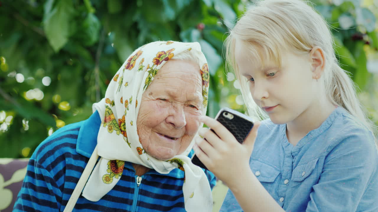 그 소녀는 세대 개념 4k 비디오의 스마트폰 친교에 할머니 사진을 보여줍니다