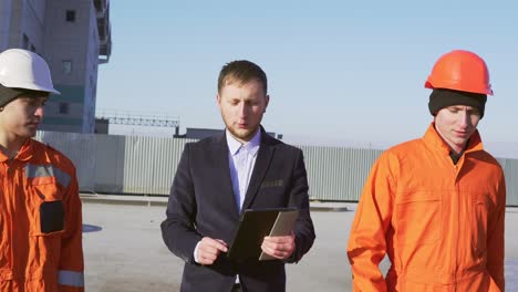 engineer in a suit and two workers in orange uniform and helmets are walking through building facility. shot in 4k