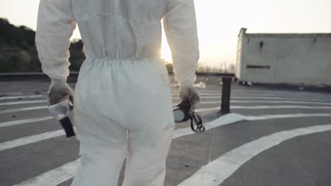 Unrecognizable-worker-in-protective-suit-walks-with-mask-and-respirator-in-hands