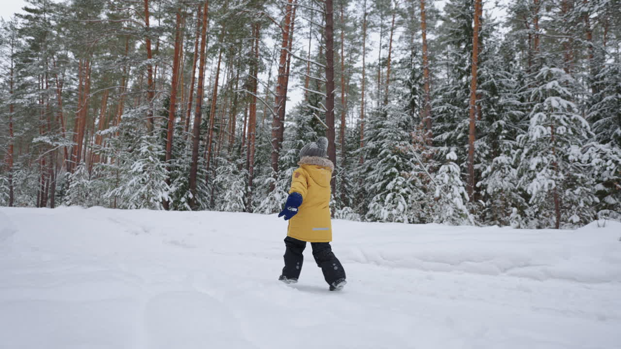 un niño pequeño de 3-4 años corre en el bosque de invierno una vista desde atrás en cámara lenta en una chaqueta amarilla. el concepto de diversión de invierno y recreación activa libertad y una infancia feliz