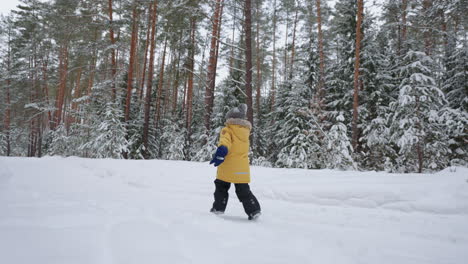 A-little-boy-of-3-4-years-old-runs-in-the-winter-forest-a-view-from-the-back-in-slow-motion-in-a-yellow-jacket.-The-concept-of-winter-fun-and-active-recreation-freedom-and-a-happy-childhood