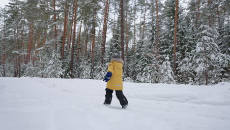 a little boy of 3-4 years old runs in the winter forest a view from the back in slow motion in a yellow jacket. the concept of winter fun and active recreation freedom and a happy childhood
