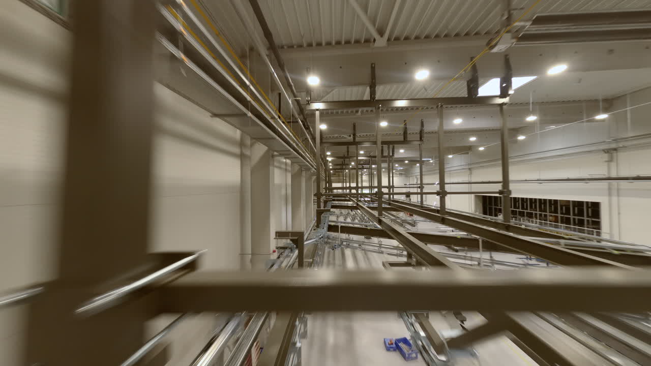 FPV-droneoptagelser, der flyver dynamisk gennem transportsystemerne på en pulverlakeringfabrik. Kameraet snoer sig mellem ophængte metaldele, der bevæger sig langs produktionslinjer, og fanger den industrielle stemning