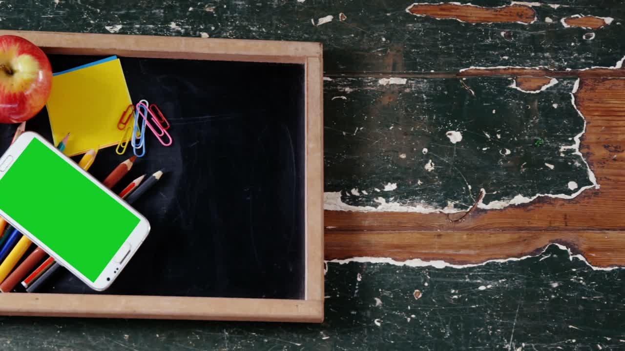 яблоко и мобильный телефон со школьными принадлежностями на сланце