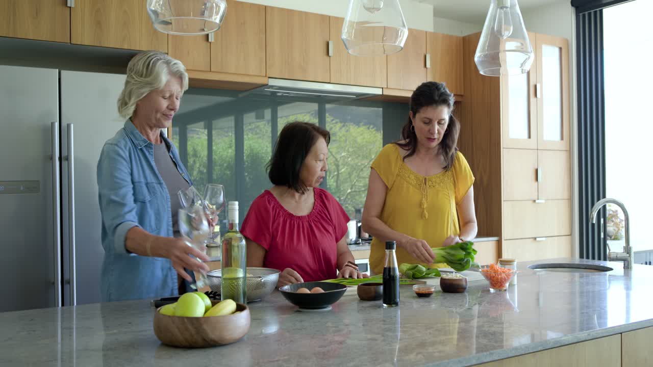 Mulheres diversas, incluindo uma idosa, abrindo a geladeira, pegando vinho, picando salada e servindo na bancada da cozinha para uma refeição.