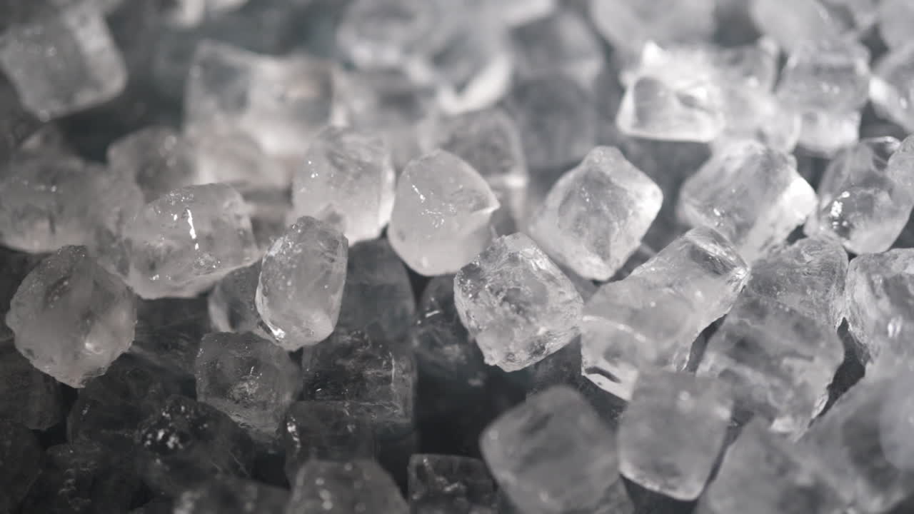 Blocks of ice being shoveled and pushed around by white male bartenders' hand in slow motion