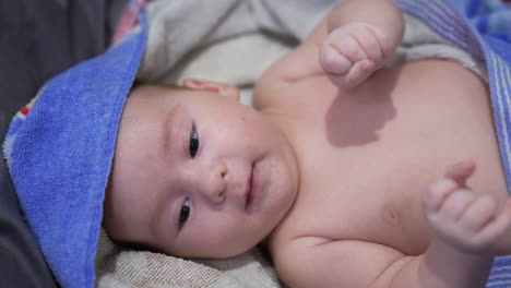 washed and happy little toddler wrapped in towel lying on the bed. lovely child tossing feet and little fists. close up.