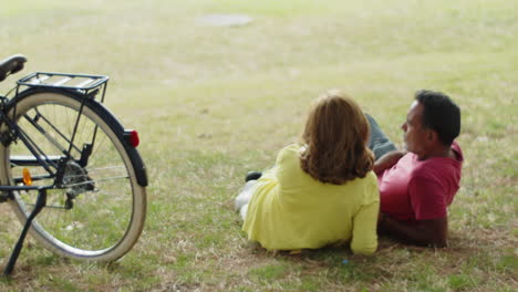 Back-view-of-senior-couple-lying-on-lawn-in-summer-park