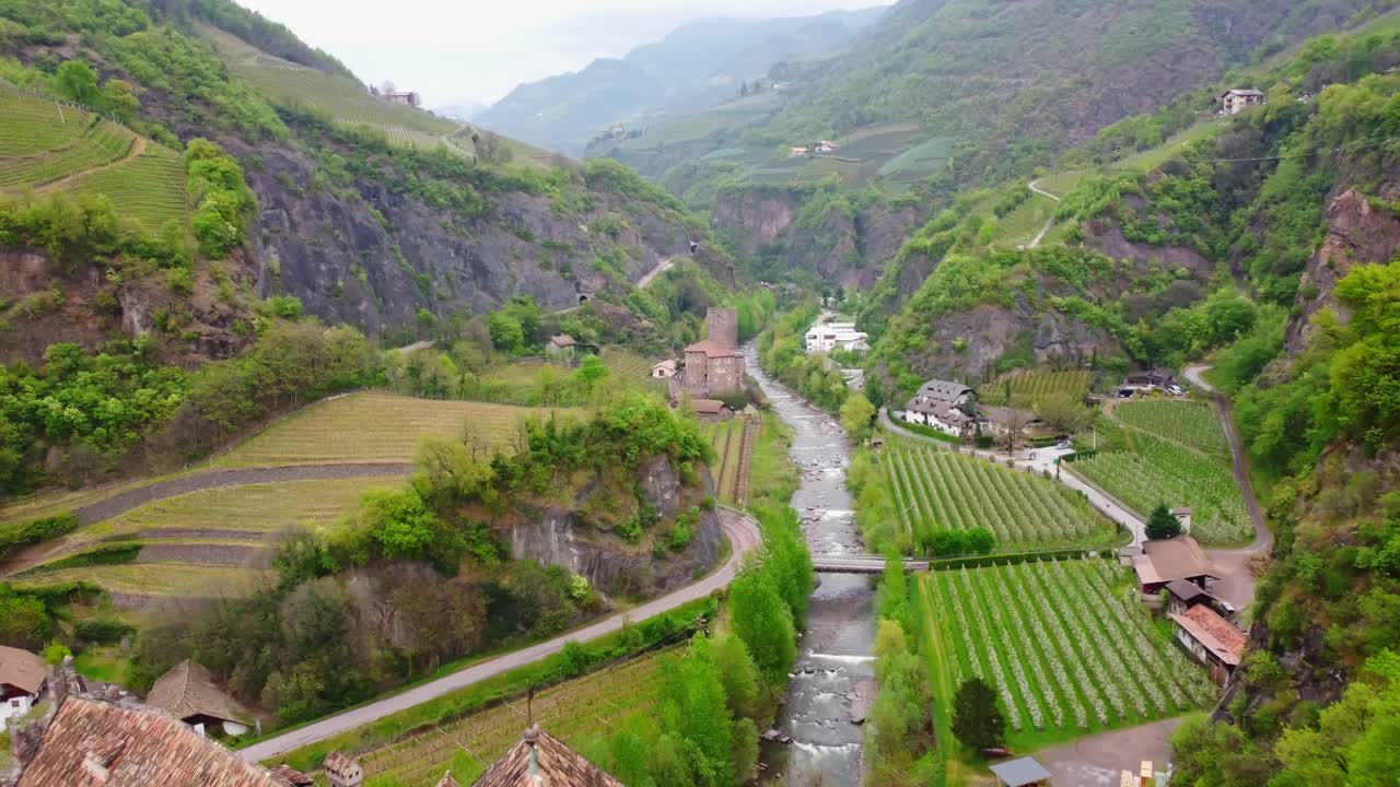 Scenic view of vineyards, mountains, and river around the historic Castel Roncolo in Bolzano