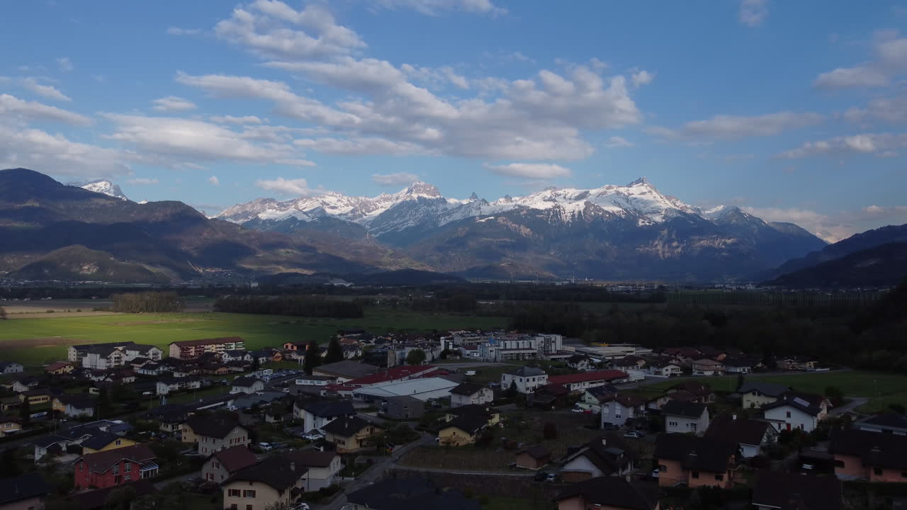 Slow aerial tilt down above Vionnaz, Switzerland with the snow covered Alps in the distance.