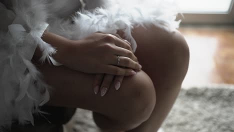 delicate hands resting on a soft, feathered robe, showcasing a subtle engagement ring