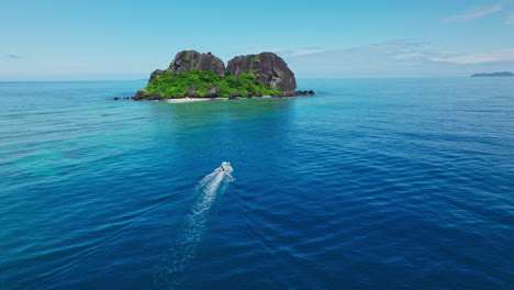 aerial tracking of tour boat heading toward lush tropical island in crystal clear waters