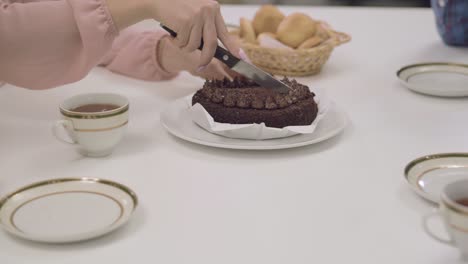 close-up of a delicious chocolate cake at the table. female caucasian hands cutting tasty dessert in four pieces. family dinner.