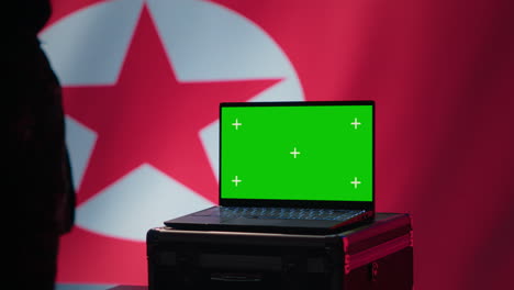 un agente de la policía secreta de corea del norte usa herramientas de propaganda en una computadora portátil de pantalla verde.