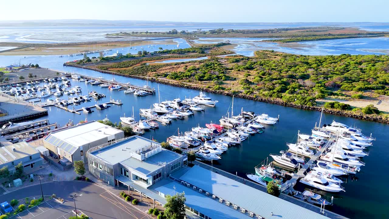Aerial footage of Queenscliff Marina, showcasing boats, a lighthouse, and coastal scenery in bright daylight