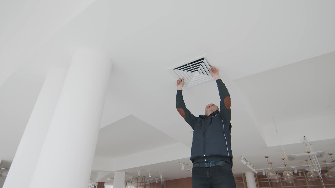 el maestro se para en una escalera en la habitación sin reparación y repara el aire acondicionado. habitación sin reparaciones y un especialista trabajando en la escalera