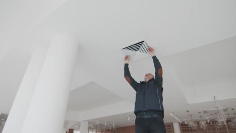 master stands on a ladder in the room without repair and repairs the air conditioner. room without repair and a specialist working on the ladder