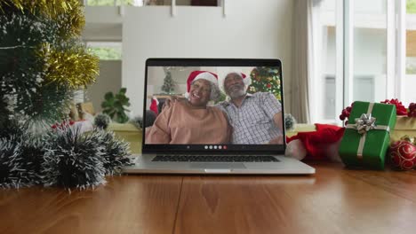 Smiling-african-american-couple-wearing-santa-hats-on-christmas-video-call-on-laptop