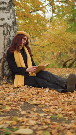 el estudiante de boina amarilla se relaja leyendo bajo los árboles de otoño, rodeado por una alfombra de hojas secas, encarnando la atmósfera serena del otoño.
