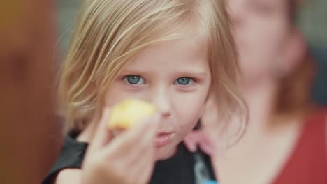 A-close-up-slowmo-shot-of-a-blue-eyed-blonde-girl-eating-a-peach-and-showing-it-into-the-camera