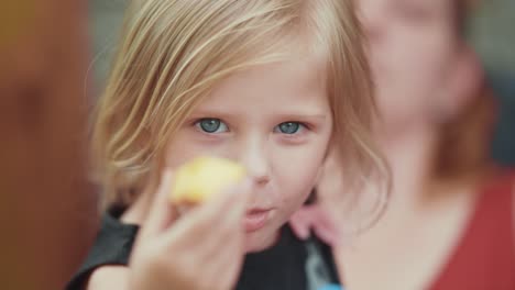 a close-up slowmo shot of a blue-eyed blonde girl eating a peach and showing it into the camera