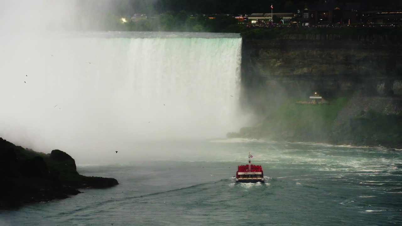 A red-decked tour boat cruises toward the thundering Horseshoe Falls at Niagara, cutting through mist and river currents as crowds gather on the cliffs above