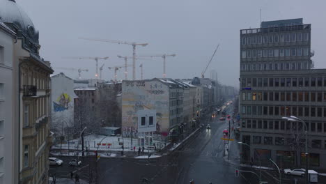 Low-traffic-on-road-intersection-in-winter-city.-Group-of-tower-cranes-on-construction-site-in-background.--Berlin,-Germany