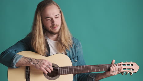 un joven caucásico tocando la guitarra ante la cámara.
