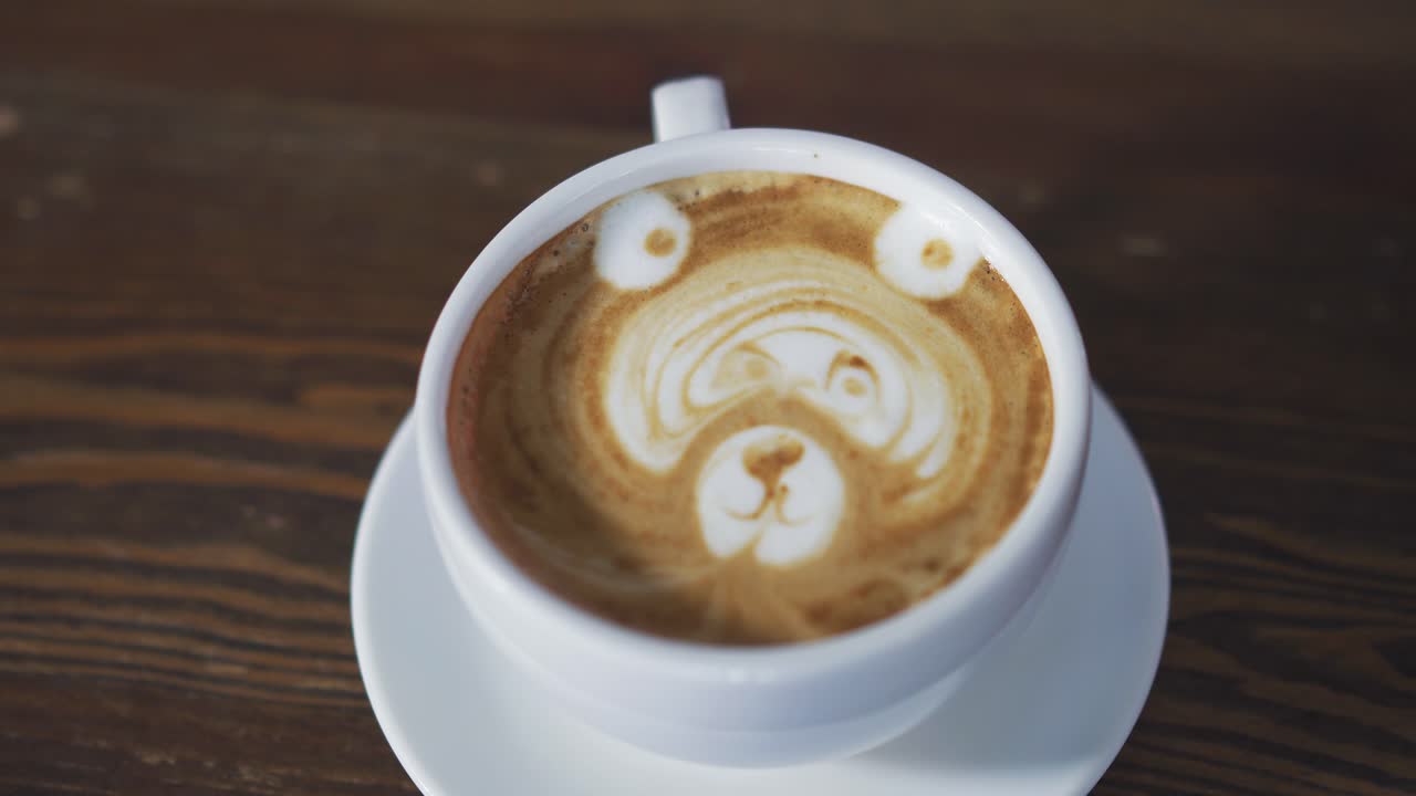 Man's hands turning a cup of coffee with latte art to show the drawing in the form of a bear. Cappuccino, latte art