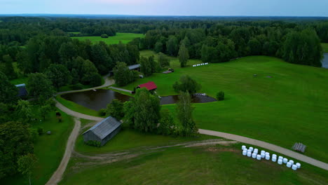 cinematic aerial shot of a small hut with a red roof on a little lake among green grass fields and trees, aerial